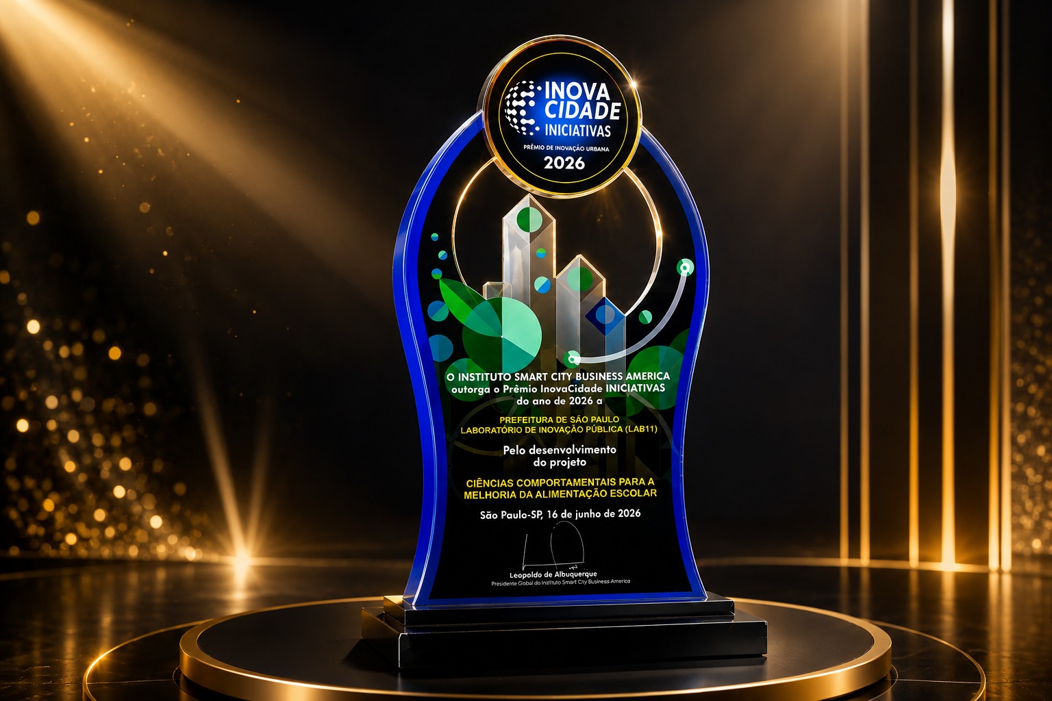 #ParaTodosVerem: A imagem mostra um troféu do Prêmio InovaCidade Iniciativas 2026, concedido à Prefeitura de São Paulo, por meio do Laboratório de Inovação Pública (LAB11), pelo projeto “Ciências Comportamentais para a Melhoria da Alimentação Escolar”. O troféu possui detalhes em azul e está em destaque sobre uma base preta, com fundo escuro e iluminação dourada, reforçando a ideia de reconhecimento e inovação na gestão pública.